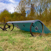 DD Superlight Tarp Small set up in a grassy field next to a bicycle, showcasing its lightweight design.